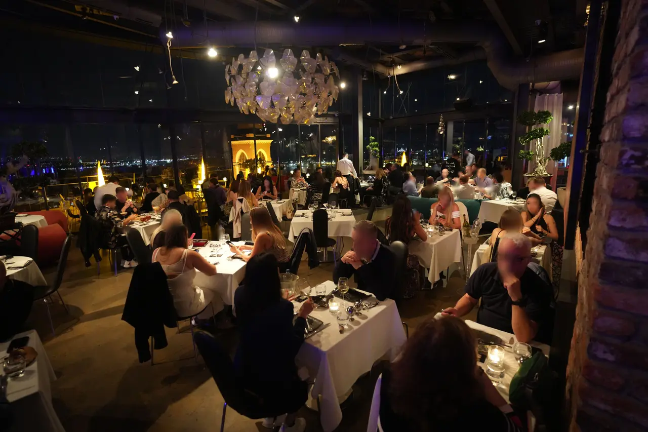 Guests dining at night in the 360 Istanbul restaurant beneath the signature chandelier, with the illuminated bell tower of Saint Antoine Church visible through the windows