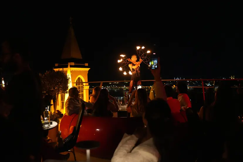 Gece terasta ateş performansı; arkada ışıklı Saint Antoine Kilisesi çan kulesi