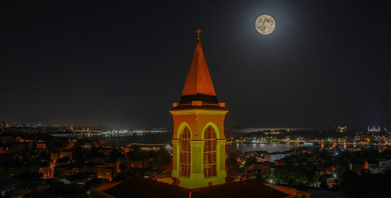 360 İstanbul'dan görülen ışıklı Saint Antoine Kilisesi çan kulesi ve İstanbul siluetinin üzerinde dolunay