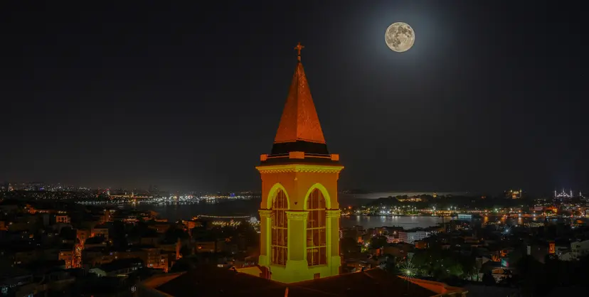 360 İstanbul'dan görülen ışıklı Saint Antoine Kilisesi çan kulesi ve İstanbul siluetinin üzerinde dolunay